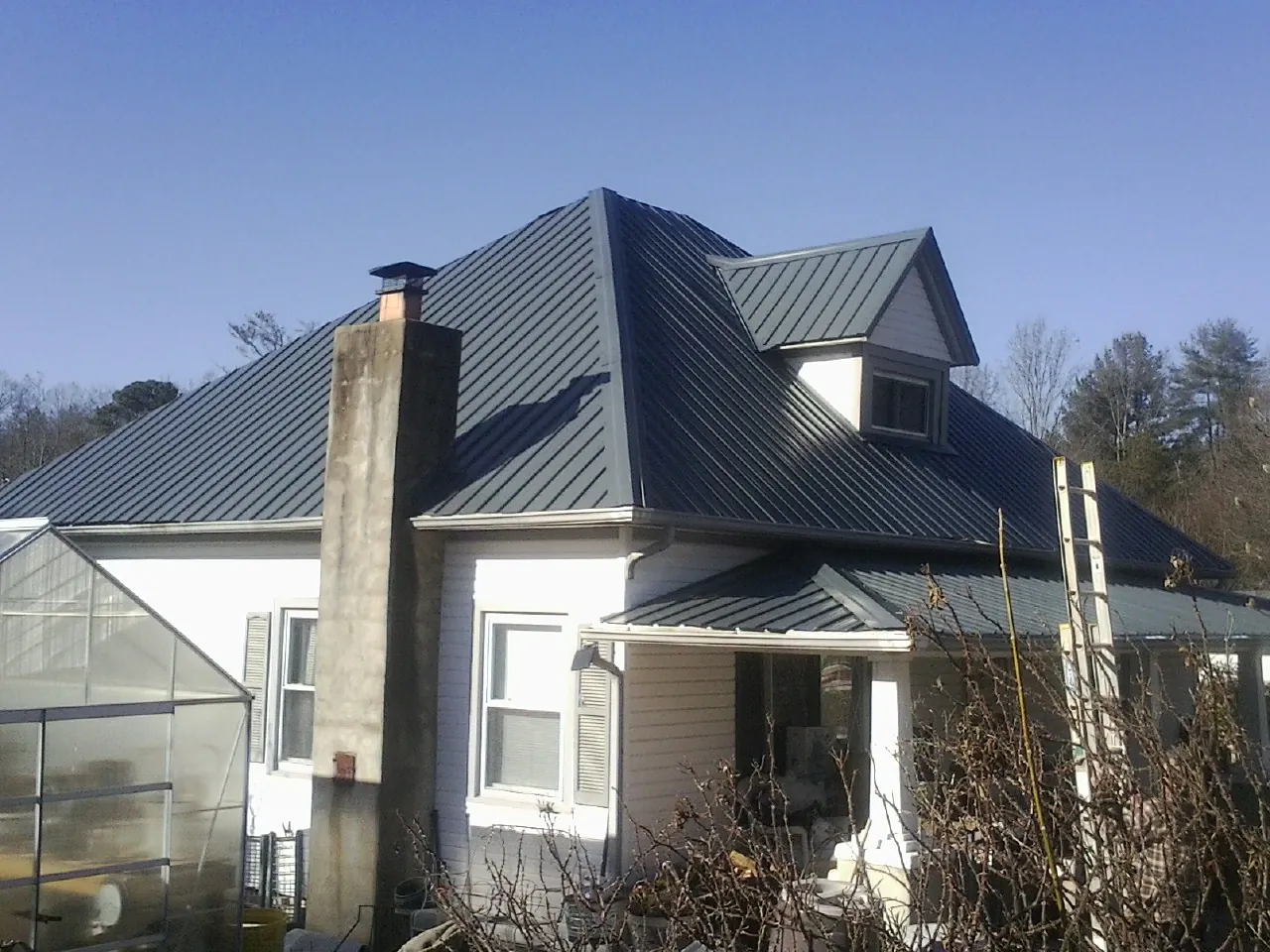 Dark blue standing seam metal roof on a white farmhouse with dormer — Slate & Tile Roof Repair by Roofing Brothers in Kinsman