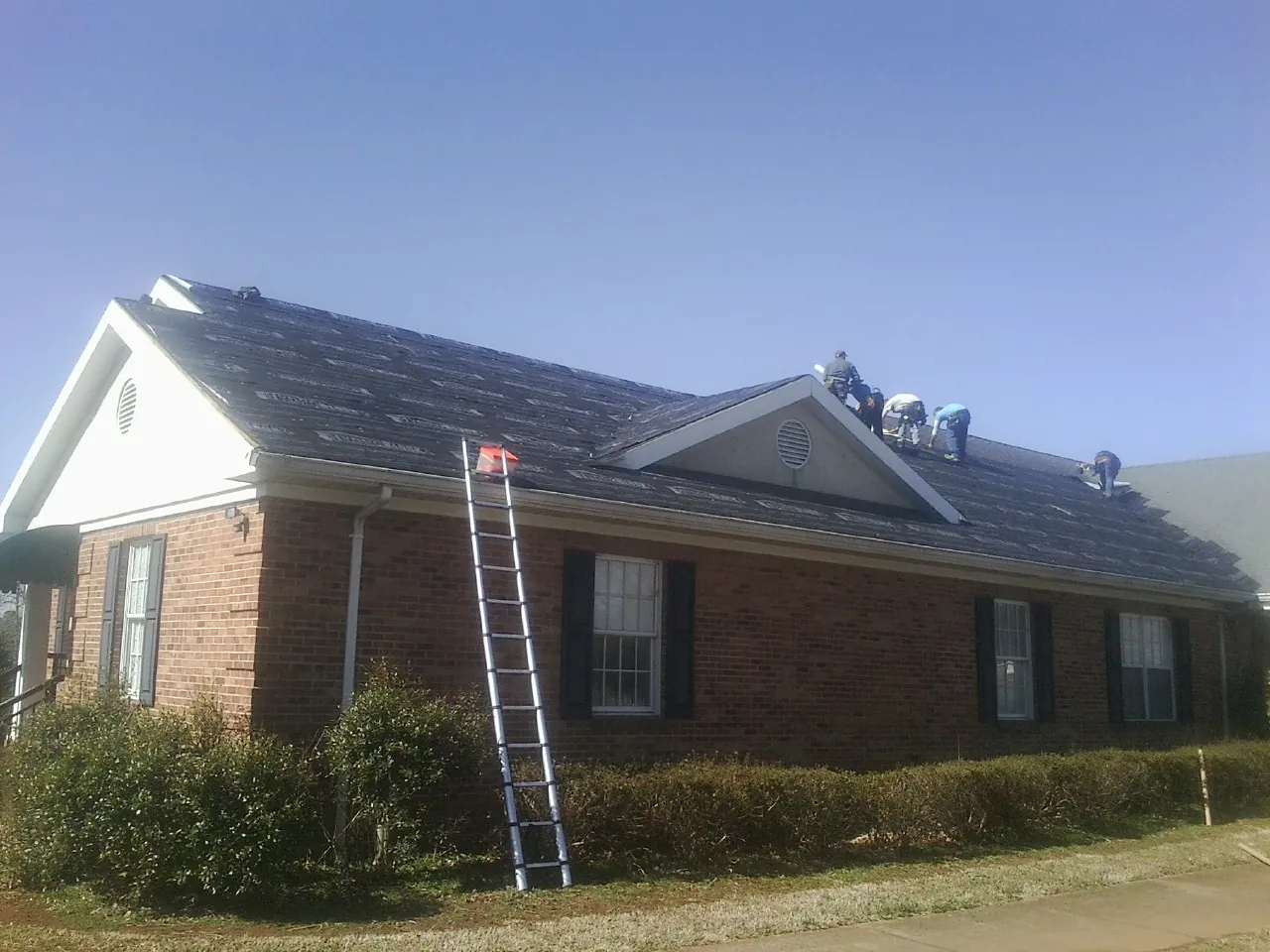 Crew tearing shingles off a brick ranch roof with a ladder set — Metal Roof Repair work by our crew in Kinsman