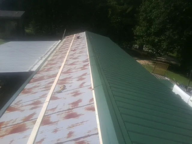Old rusted panels beside newly installed green metal roofing — Wind Damage Roof Repair by Roofing Brothers in Kinsman