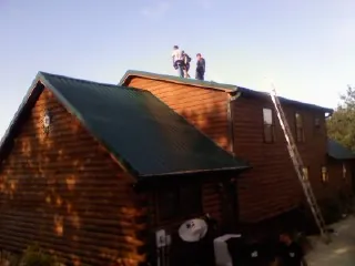 Crew on the ridge of a green metal roof on a two story log home in Kinsman