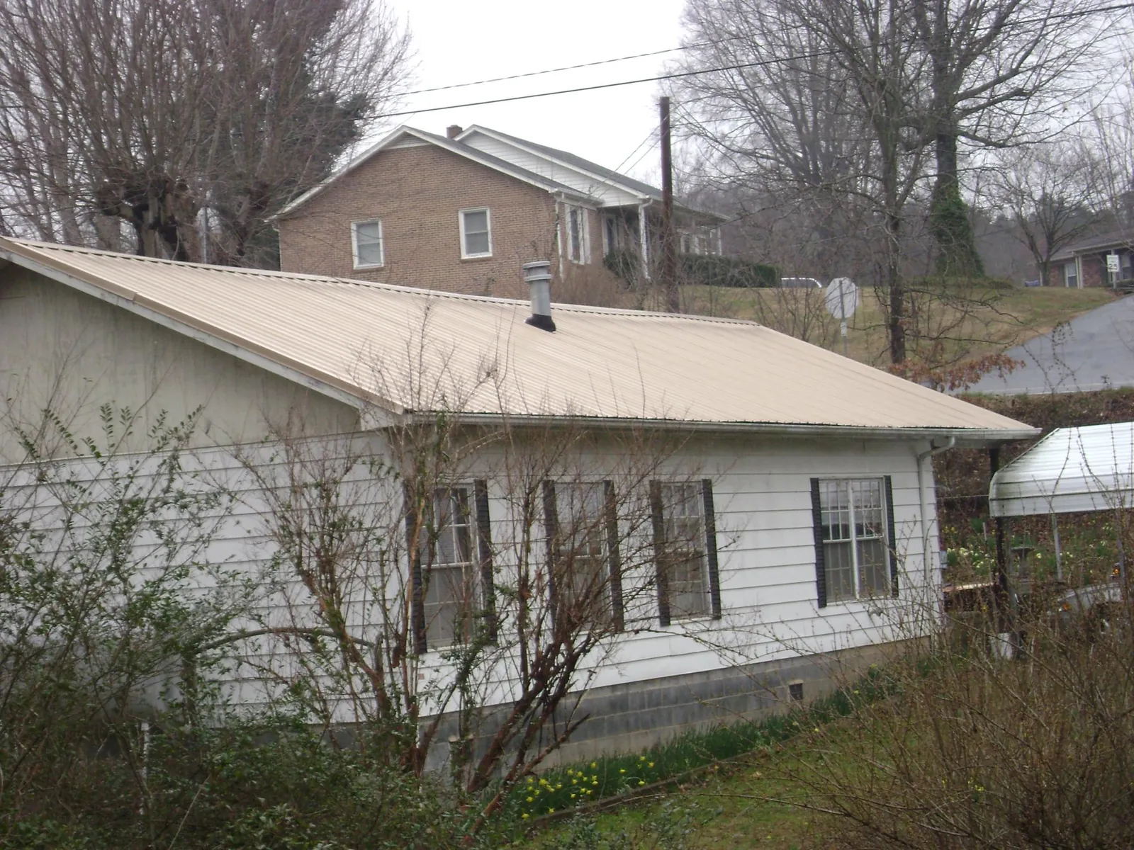 Tan metal roof on a white sided house set into a hillside — Commercial Roofing by Roofing Brothers in Kinsman
